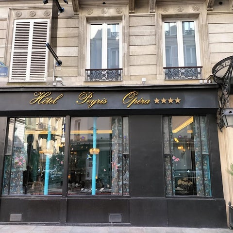 The Hotel Peyris Opéra's facade displays a dark awning with gold lettering and a glimpse of the lobby interior.
