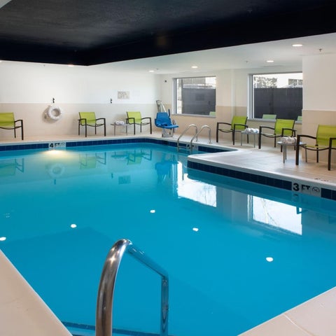 An indoor pool with blue water and several green chairs surrounding the pool deck.