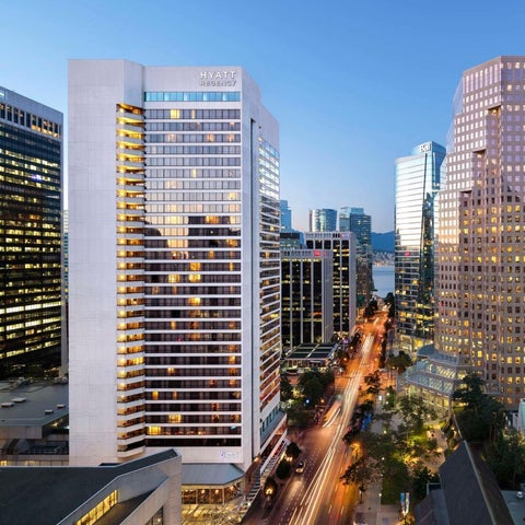 An elevated view showcases a modern hotel building with illuminated windows alongside a busy city street at dusk.