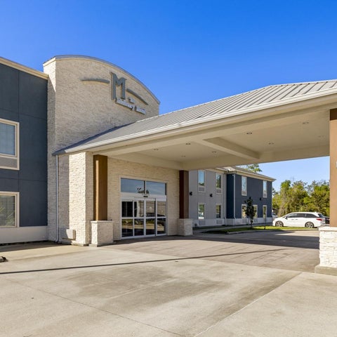 A modern hotel building features a curved facade with a prominent logo and a covered entryway with a concrete driveway.