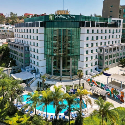 An aerial view showcases a Holiday Inn hotel with a swimming pool, lush landscaping, and modern architecture.