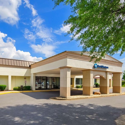 A Best Western hotel facade features a covered entrance with columns and well-maintained landscaping under a partly cloudy sky.