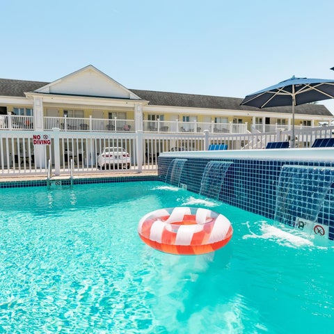 A blue tiled pool with a red and white inflatable ring floats in the water, next to a hotel and patio.