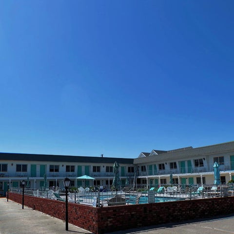 A hotel features an outdoor pool area with lounge chairs, umbrellas, and a brick fence surrounding the pool.