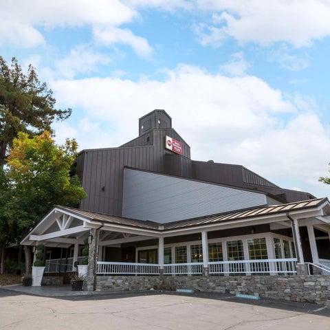 A multi-story building with a sloped roof and a covered entrance area with white railings and landscaping.