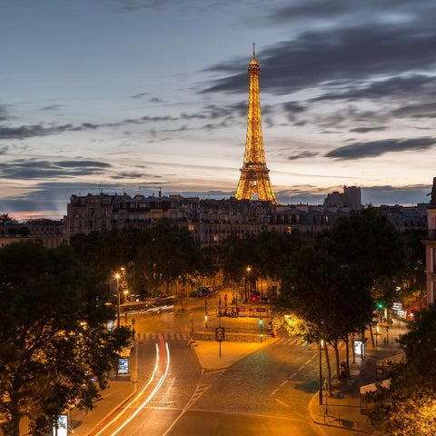 The Eiffel Tower rises above the Parisian cityscape at dusk, with illuminated streets and buildings below.