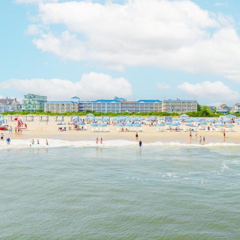 A wide view of a crowded beach with numerous people enjoying the water and sun under a partly cloudy sky.