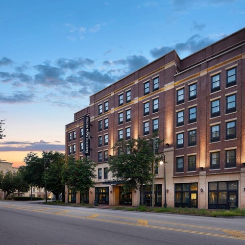 A brick building with multiple stories and windows stands on a street corner at dusk, illuminated by exterior lighting.