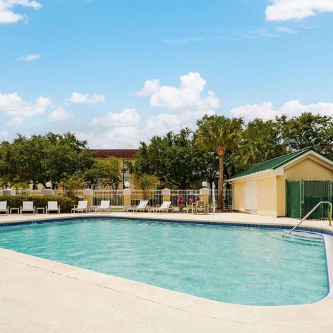 A rectangular swimming pool with lounge chairs surrounds it, set against a backdrop of lush trees and a partly cloudy sky.