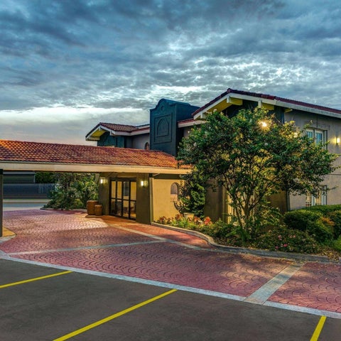 A multi-story hotel building with a brick-paved driveway and landscaping, illuminated by outdoor lighting under a cloudy sky.