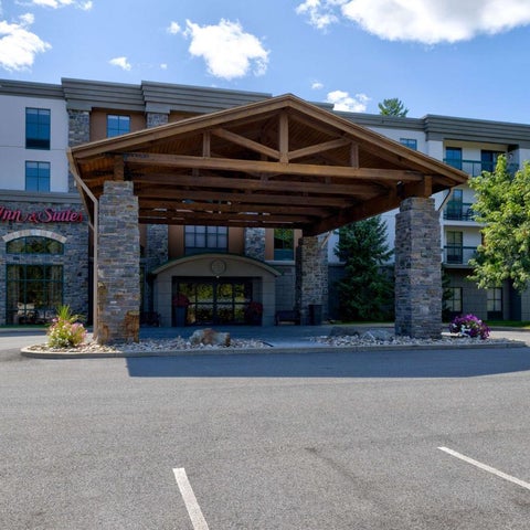A Hampton Inn hotel features a large wooden portico over the entrance and a multi-story building with a stone facade.