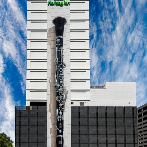 A tall Holiday Inn hotel building features a large, vertical sculpture of a clarinet on its facade.