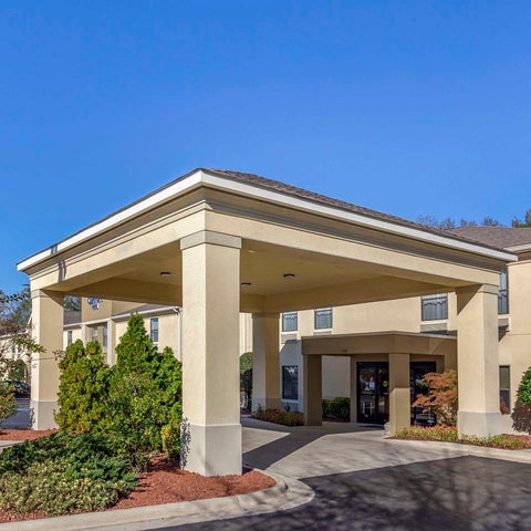 A beige hotel building features a covered entrance with large columns and landscaping in front of it.
