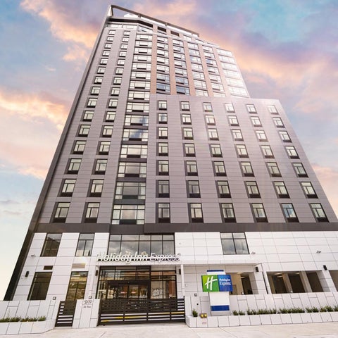 A modern, tall hotel building with a gray and white facade stands against a colorful sunset sky.