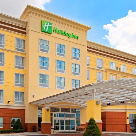A yellow Holiday Inn hotel building with a covered entrance and multiple windows under a partly cloudy sky.