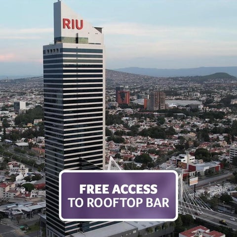 A tall, modern hotel building with a rooftop bar is seen against a sprawling cityscape under a hazy sky.