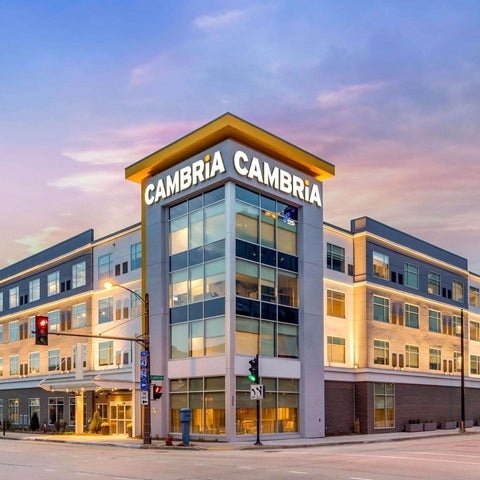 A modern hotel building with the name 'Cambria' prominently displayed on its facade under a cloudy sky.