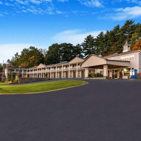 A motel with a sign reading 'welcome to lake george' sits on a manicured lawn with trees and a building in the background.