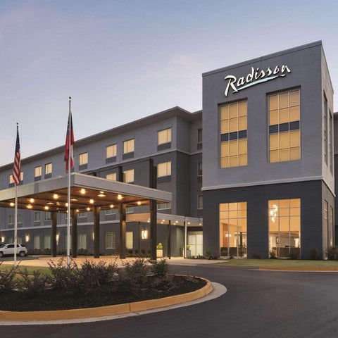 A Radisson hotel building facade with a covered entrance, parking lot, and American flags in the foreground.
