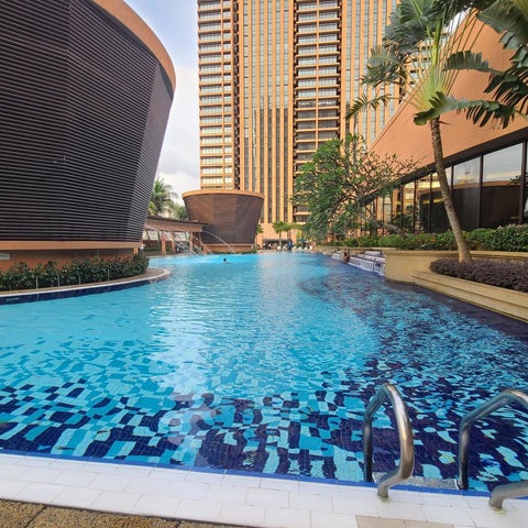 A large, blue, tiled pool with a modern, curved building and lush greenery in the background.
