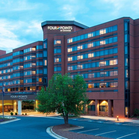 A Four Points by Sheraton hotel building is shown at dusk with trees, parking, and flags in the foreground.