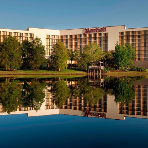 A large Marriott hotel building with a pond reflecting the structure and surrounding trees under a clear sky.
