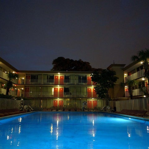 An illuminated pool reflects the lights of a surrounding motel building at dusk.