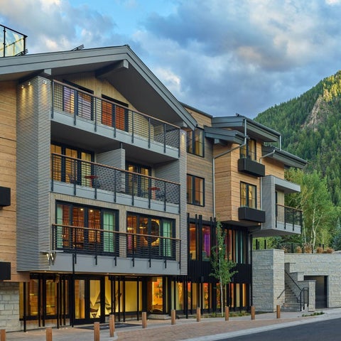 A modern apartment building with a wooden facade and balconies overlooks a forested mountain landscape at dusk.