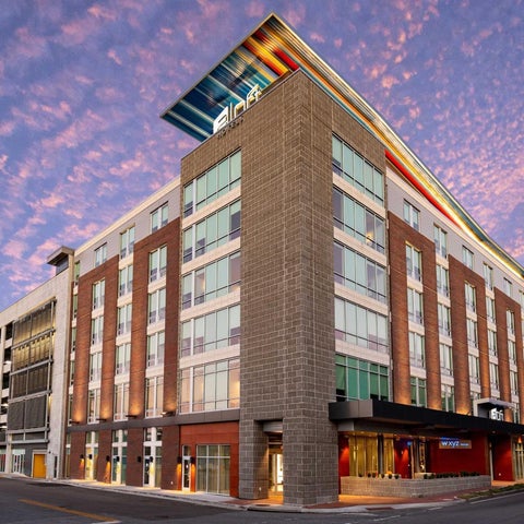 A modern brick building with colorful accents and a parking garage is captured at dusk with a vibrant sky.
