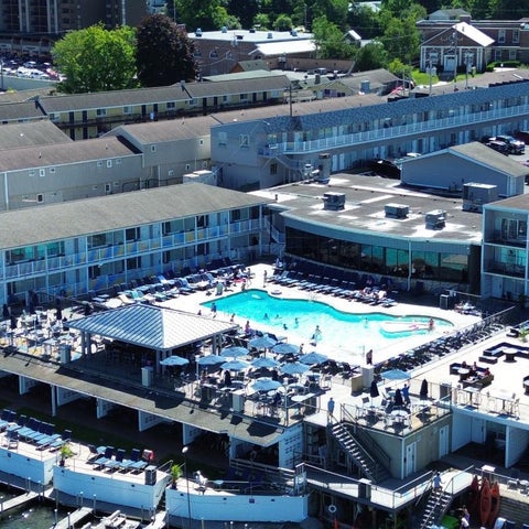 An aerial view shows a hotel with a large outdoor pool, lounge chairs, and a patio overlooking a waterway.