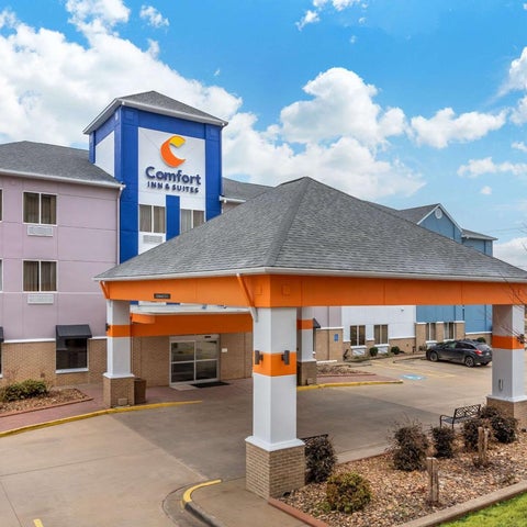 A Comfort Inn & Suites building features a covered entryway, parking lot, and American flag against a cloudy sky.