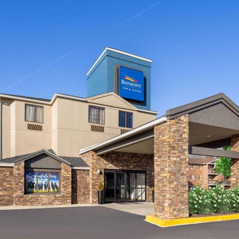 A Baymont Inn & Suites building features a brick facade, covered entrance, and a blue and white logo against a clear sky.