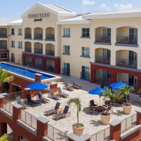 An aerial view showcases a Courtyard by Marriott hotel with a pool, patio seating, and lush landscaping.