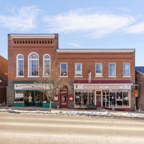 A two-story brick building with storefronts displaying merchandise and signage under a partly cloudy sky.