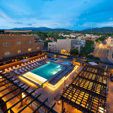 An elevated view showcases a rectangular pool surrounded by lounge chairs and shaded seating areas on a rooftop terrace.