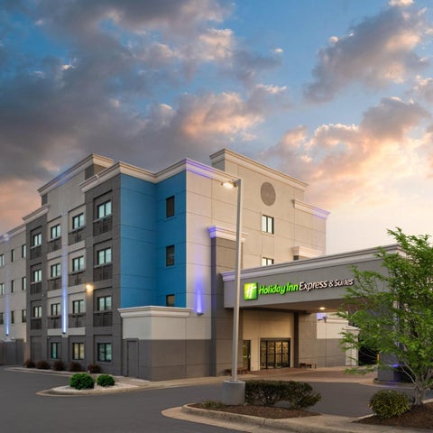 A Holiday Inn Express & Suites building is shown with a modern facade and landscaping under a colorful sunset sky.
