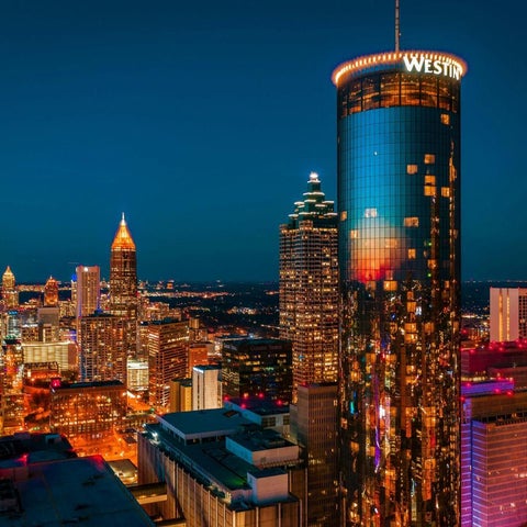 An aerial view showcases the Atlanta skyline at dusk, featuring illuminated skyscrapers and city lights.