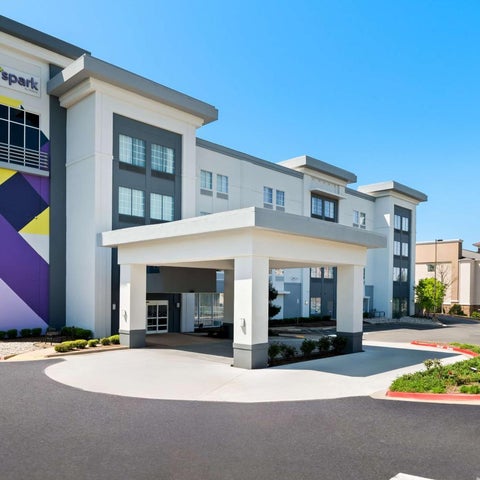 A modern hotel building with a covered entrance, colorful facade, and signage under a clear blue sky.