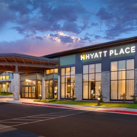 A Hyatt Place hotel exterior features a modern facade with large windows, a covered entrance, and landscaping.