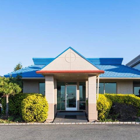 A blue and beige hotel building facade features a peaked roof, entrance, and manicured landscaping with an American flag.