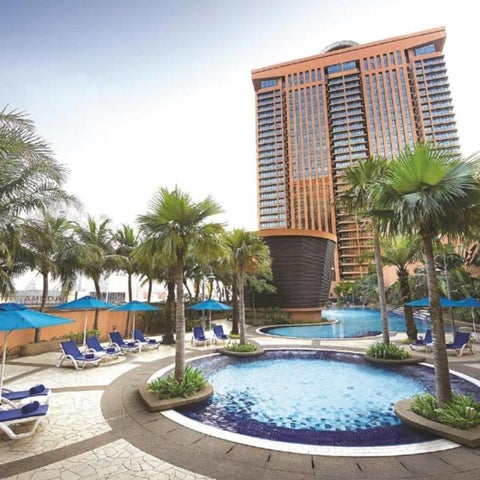 A resort pool area features lounge chairs, umbrellas, palm trees, and a modern high-rise building in the background.