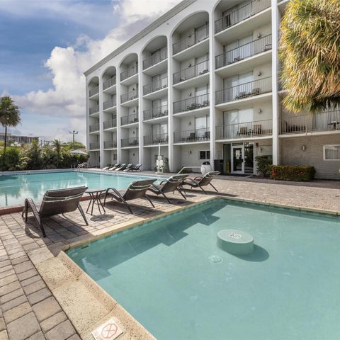 A rectangular swimming pool with lounge chairs and a multi-story building with balconies in the background.