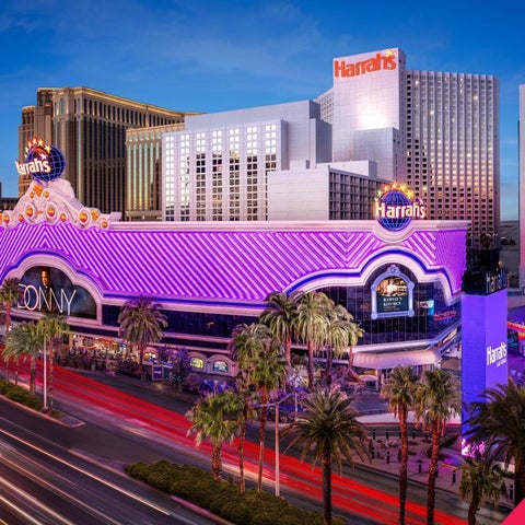 A brightly lit nighttime view of the Harrah's Las Vegas hotel and casino, showcasing its facade and surrounding palm trees along the Strip.