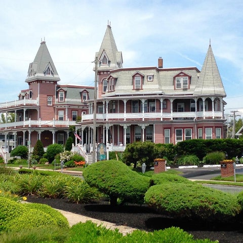 A large, ornate Victorian-style mansion with multiple turrets and a wrap-around porch sits behind manicured landscaping.