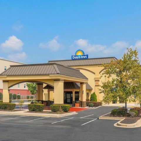 A Days Inn hotel features a covered entrance, parking lot, and landscaping under a partly cloudy sky.