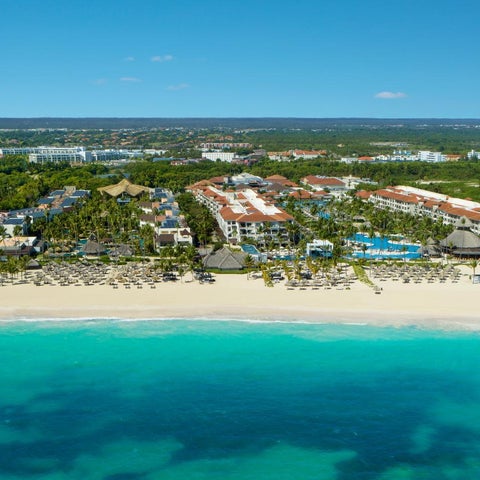An aerial view showcases a sprawling resort with multiple pools and a long stretch of white sand beach and turquoise water.