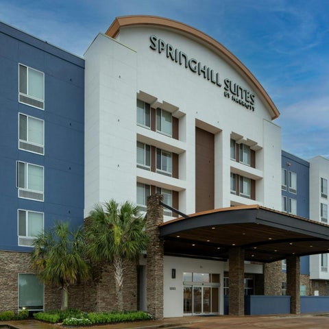 A SpringHill Suites by Marriott hotel facade features a stone base, white upper levels, and a covered entrance with landscaping.