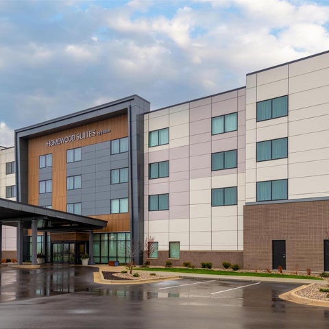 A modern, multi-story hotel building with a covered entrance and landscaped grounds under a cloudy sky.