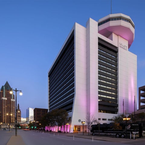 A modern hotel building with a distinctive dome is illuminated with pink lighting against a twilight sky.