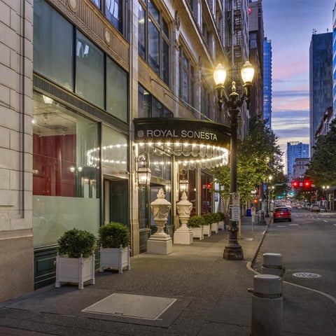 The Royal Sonesta hotel entrance features a lit awning, planters, and street lamps along a city street.